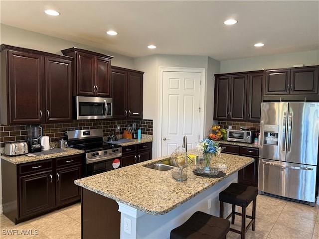 kitchen with appliances with stainless steel finishes, sink, a kitchen bar, light stone countertops, and a center island with sink