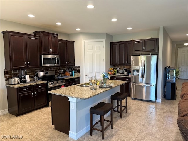 kitchen featuring dark brown cabinetry, a kitchen bar, sink, a center island with sink, and appliances with stainless steel finishes