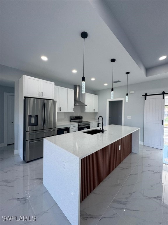 kitchen featuring appliances with stainless steel finishes, decorative light fixtures, sink, a barn door, and wall chimney range hood