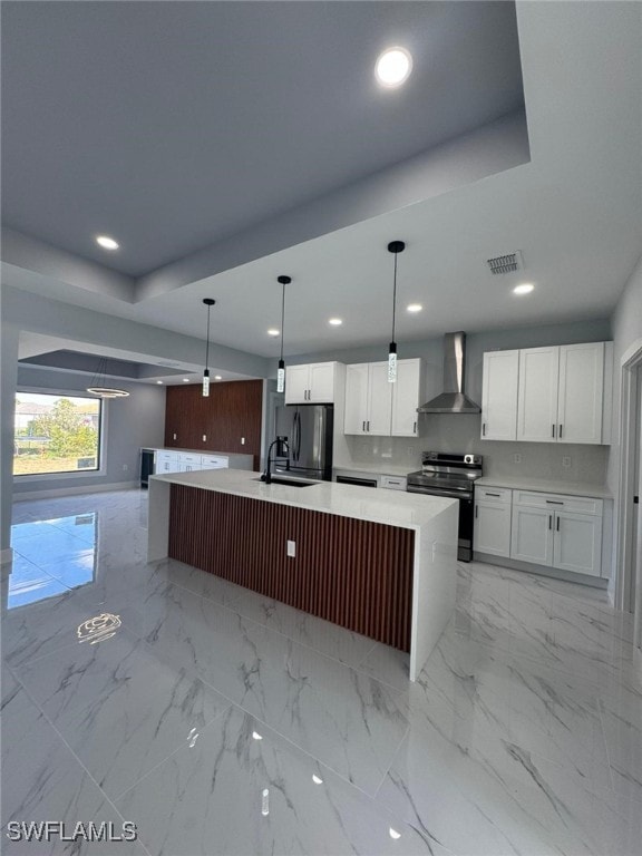 kitchen featuring white cabinetry, stainless steel electric range oven, a center island with sink, hanging light fixtures, and wall chimney range hood