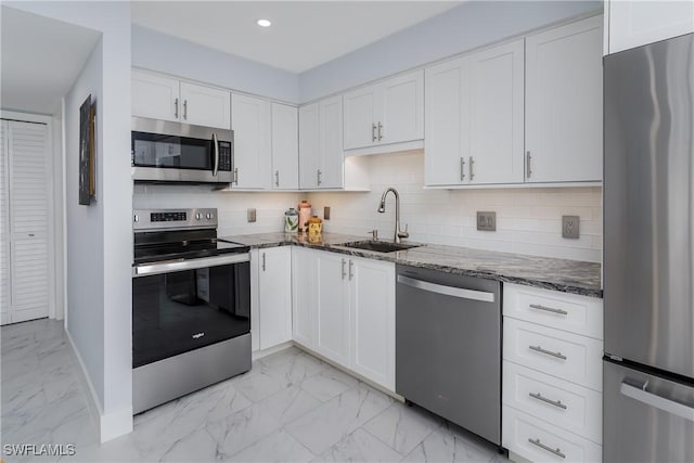 kitchen with sink, appliances with stainless steel finishes, white cabinetry, dark stone countertops, and decorative backsplash