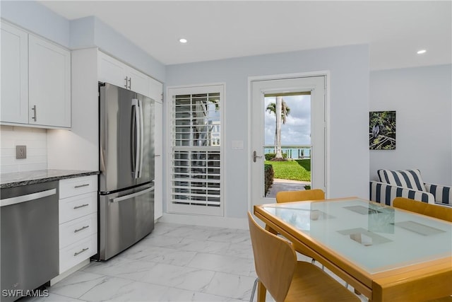 kitchen featuring white cabinetry, stainless steel appliances, backsplash, and dark stone countertops