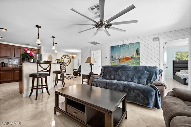 living room featuring ceiling fan with notable chandelier, light tile patterned floors, and wooden walls