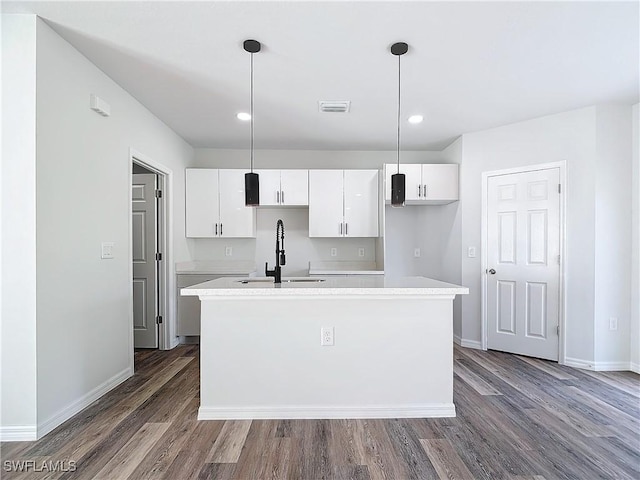 kitchen with pendant lighting, white cabinetry, sink, and a center island with sink