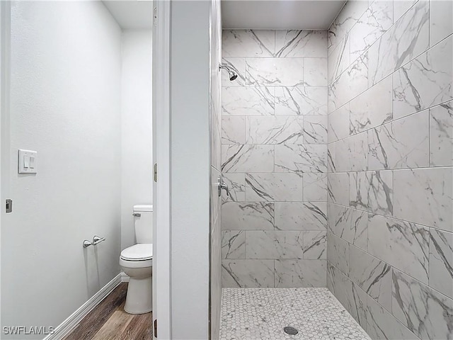 bathroom with tiled shower, toilet, and hardwood / wood-style floors