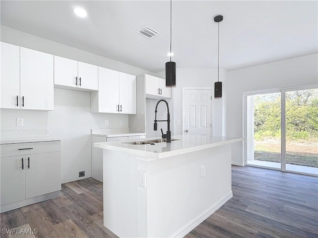 kitchen with pendant lighting, sink, dark wood-type flooring, white cabinets, and a center island with sink