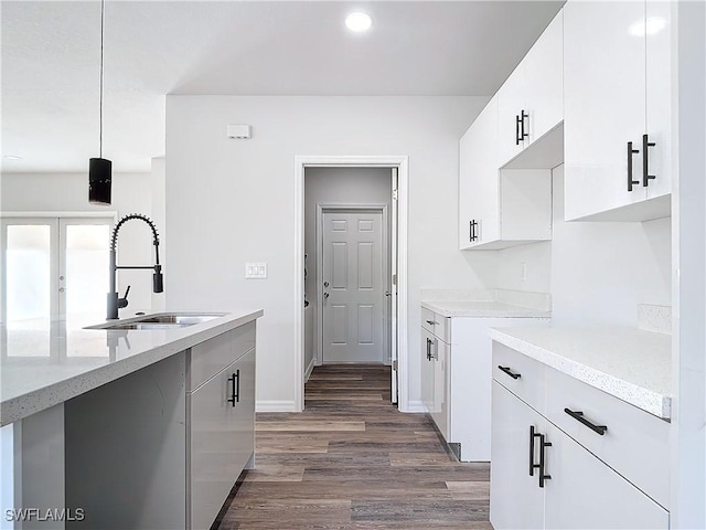 kitchen featuring dark hardwood / wood-style floors, white cabinetry, sink, hanging light fixtures, and light stone counters