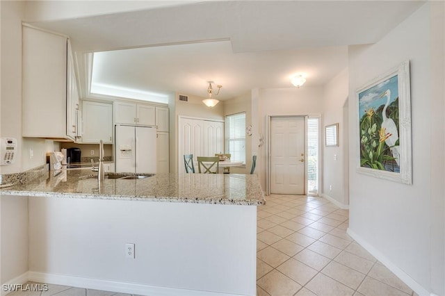 kitchen with light tile patterned floors, white refrigerator with ice dispenser, visible vents, a peninsula, and light stone countertops