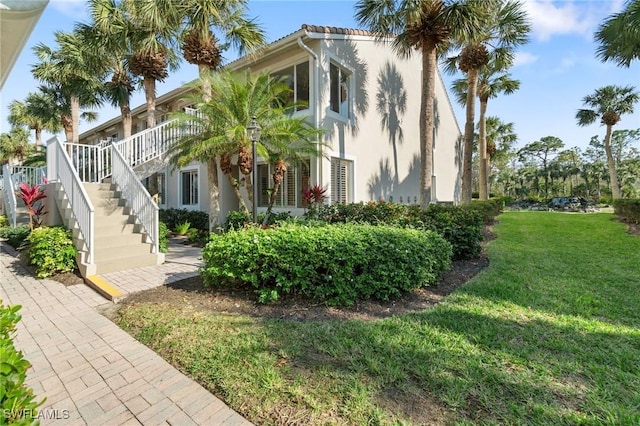 view of side of property with stucco siding, stairs, and a yard