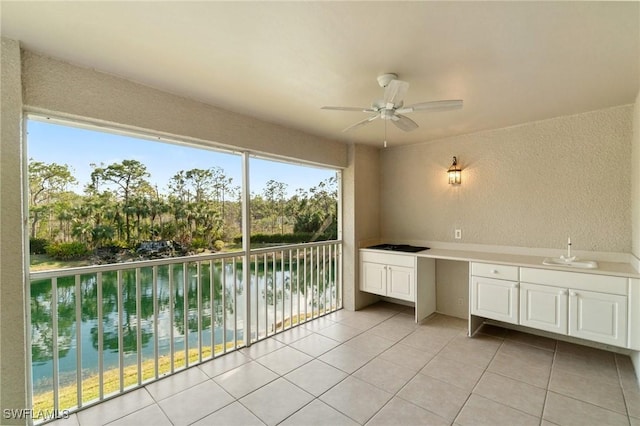 unfurnished sunroom with a water view, a ceiling fan, built in desk, and a sink