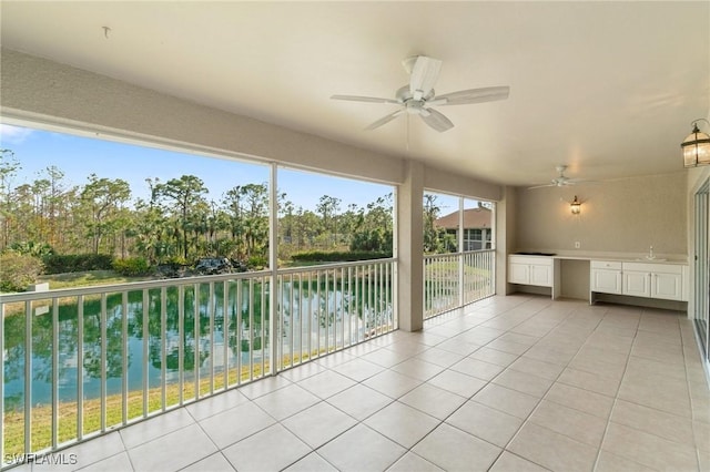 unfurnished sunroom with a water view, ceiling fan, and a sink