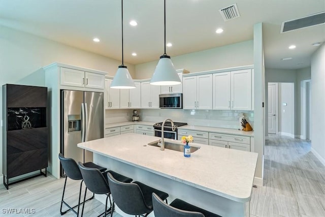 kitchen with pendant lighting, stainless steel appliances, a center island with sink, and white cabinets