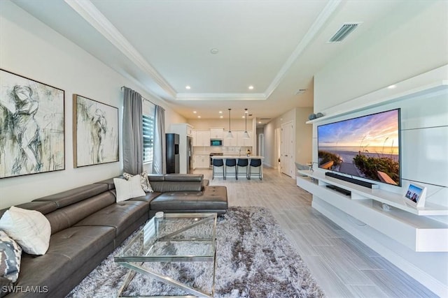 living room featuring a tray ceiling, ornamental molding, and light wood-type flooring