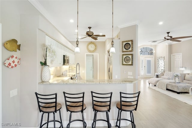 kitchen with light stone counters, stainless steel microwave, open floor plan, a breakfast bar area, and pendant lighting