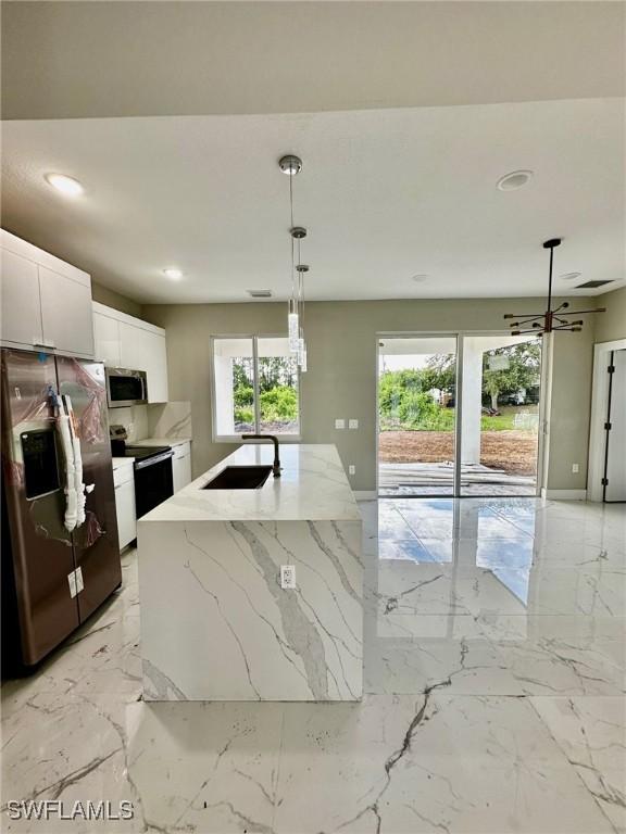 kitchen with white cabinetry, sink, hanging light fixtures, stainless steel appliances, and a center island with sink