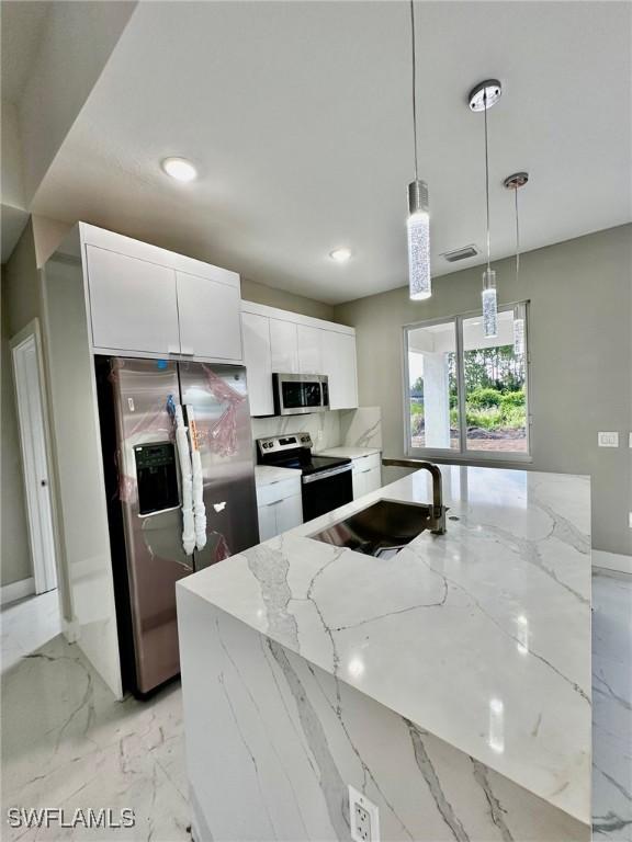 kitchen featuring decorative light fixtures, white cabinetry, sink, stainless steel appliances, and light stone countertops