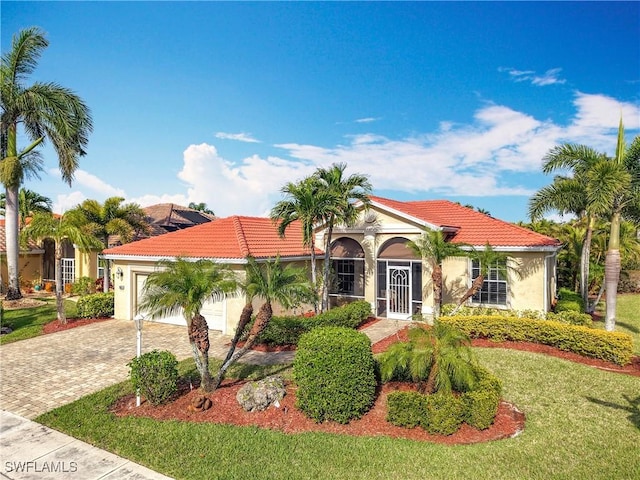 mediterranean / spanish-style home with decorative driveway, stucco siding, a garage, a tiled roof, and a front lawn