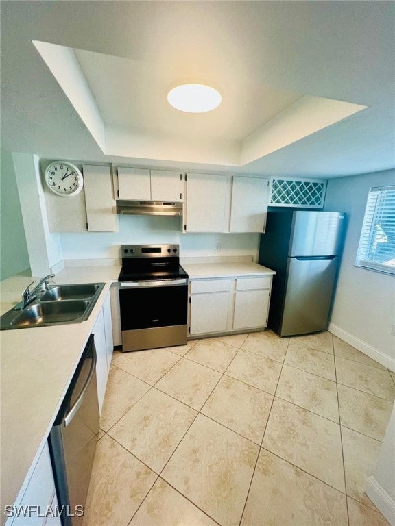 kitchen featuring appliances with stainless steel finishes, sink, white cabinets, light tile patterned floors, and a raised ceiling