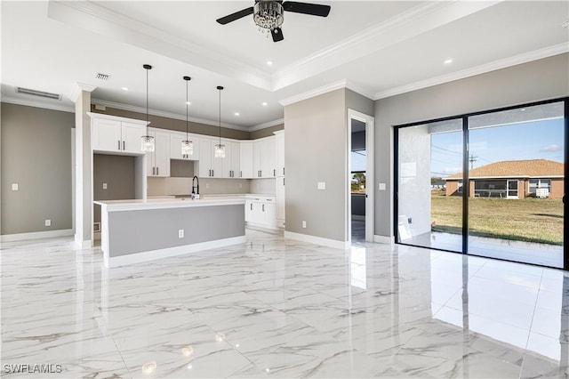 kitchen featuring decorative light fixtures, a raised ceiling, ceiling fan, a kitchen island with sink, and white cabinets