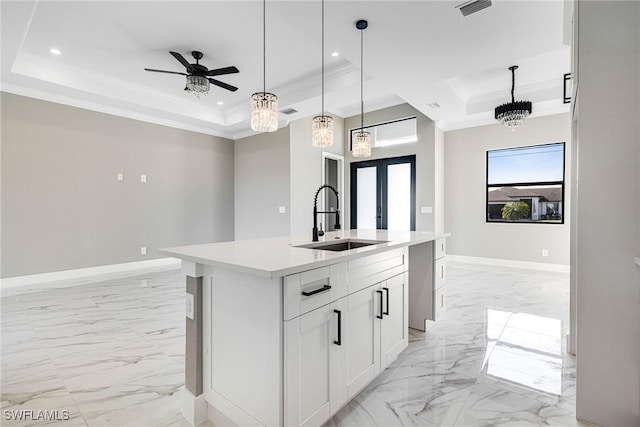 kitchen featuring sink, crown molding, white cabinetry, a center island with sink, and a raised ceiling