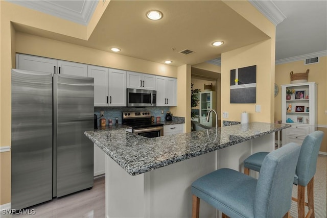 kitchen with stone counters, appliances with stainless steel finishes, white cabinets, a kitchen bar, and kitchen peninsula