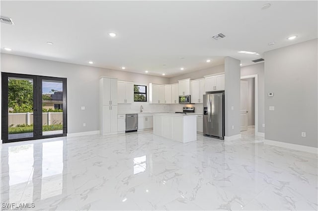 kitchen featuring french doors, white cabinetry, a kitchen island, stainless steel appliances, and backsplash