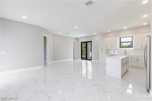 kitchen featuring sink, stainless steel refrigerator, white cabinetry, a kitchen island, and decorative backsplash