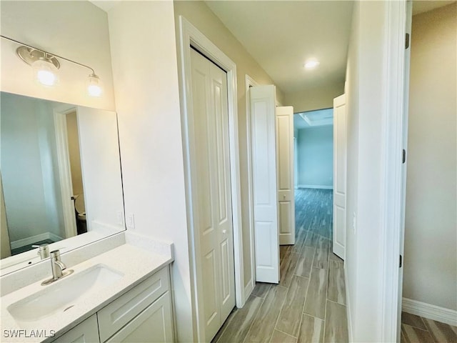 bathroom with wood finish floors, a closet, vanity, and baseboards