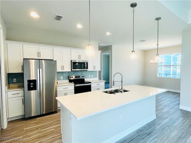 kitchen with a kitchen island with sink, stainless steel appliances, a sink, white cabinetry, and light countertops