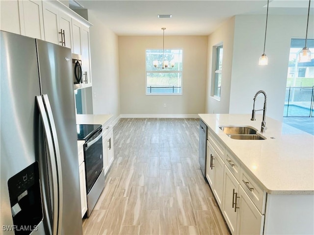 kitchen with appliances with stainless steel finishes, white cabinets, a sink, and pendant lighting