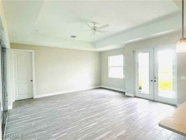 unfurnished room with a tray ceiling, french doors, wood finish floors, and baseboards