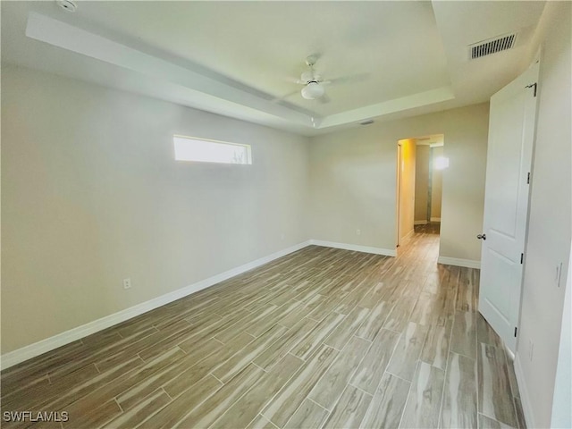 empty room with a tray ceiling, visible vents, light wood-style flooring, a ceiling fan, and baseboards