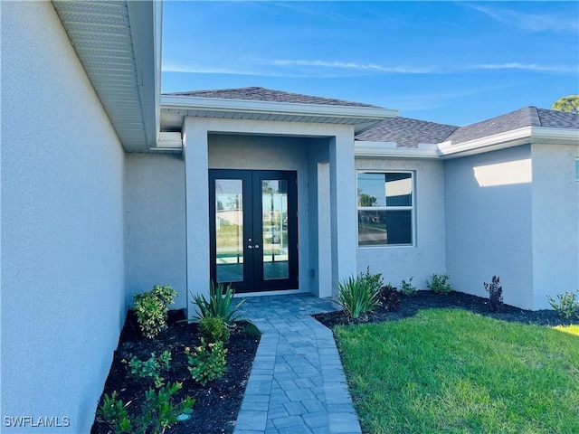 view of exterior entry with a shingled roof, french doors, a yard, and stucco siding