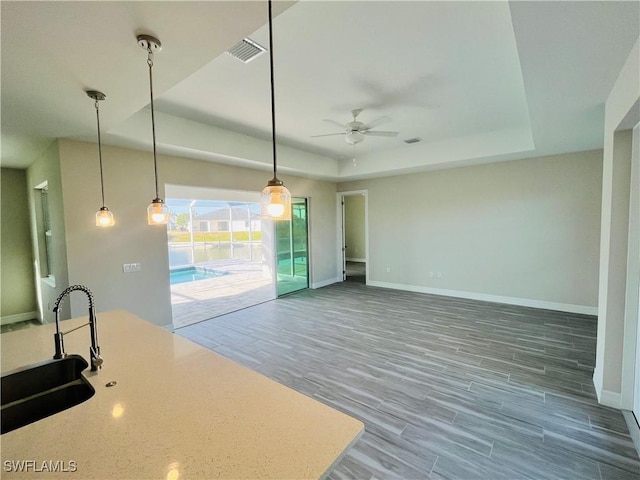 kitchen with wood finished floors, a sink, light countertops, a tray ceiling, and pendant lighting