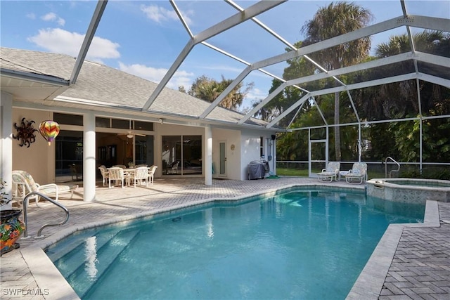 view of pool with glass enclosure, a pool with connected hot tub, a patio area, and a ceiling fan