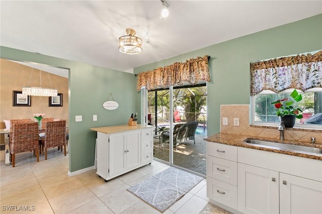 kitchen with sink, light tile patterned floors, white cabinetry, backsplash, and an inviting chandelier