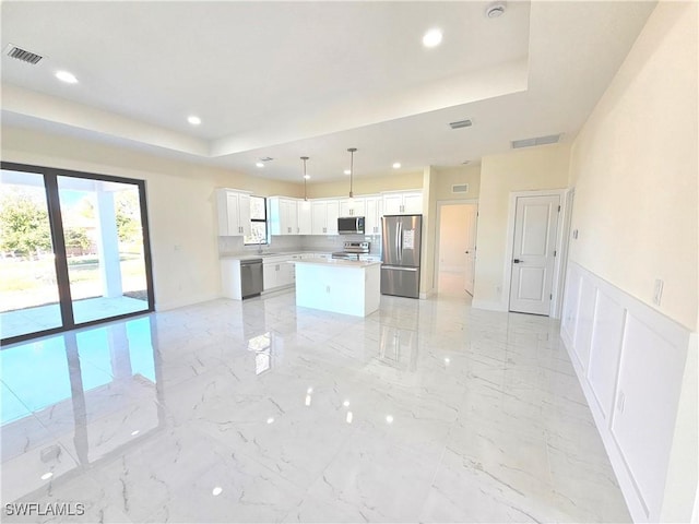 kitchen with stainless steel appliances, white cabinets, a kitchen island, decorative light fixtures, and a raised ceiling