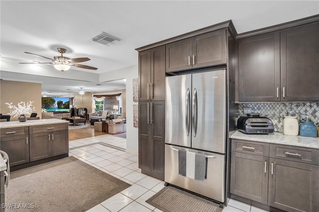 kitchen featuring light tile patterned floors, backsplash, ceiling fan, stainless steel refrigerator, and dark brown cabinetry