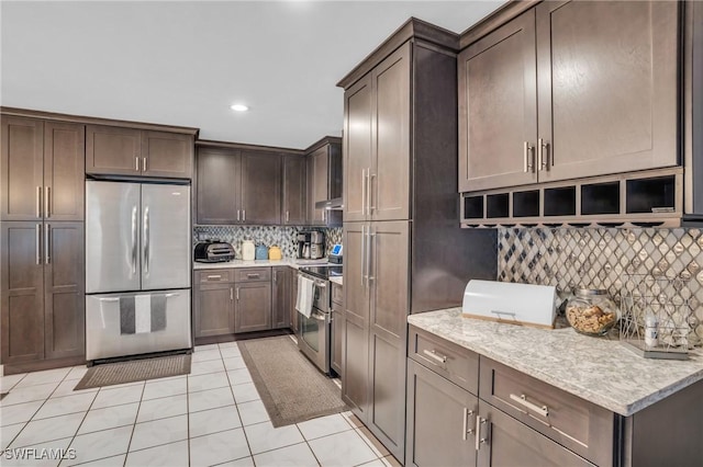 kitchen with light stone counters, light tile patterned floors, dark brown cabinets, appliances with stainless steel finishes, and backsplash