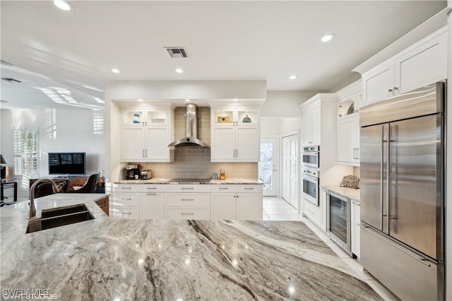 kitchen featuring wall chimney range hood, stainless steel appliances, sink, and white cabinets