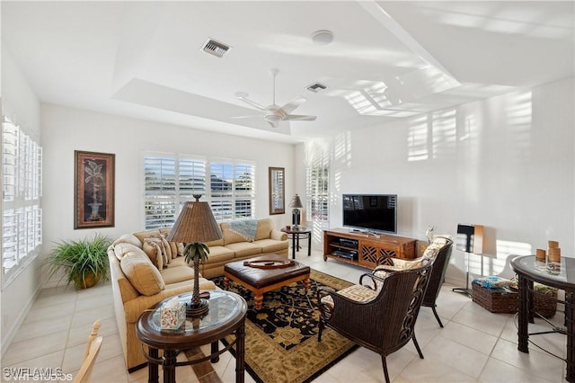 tiled living room with ceiling fan and a tray ceiling