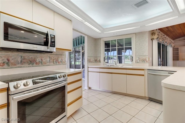 kitchen featuring appliances with stainless steel finishes, sink, backsplash, light tile patterned floors, and a raised ceiling