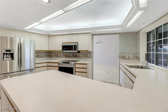 kitchen featuring appliances with stainless steel finishes, sink, white cabinets, kitchen peninsula, and a raised ceiling