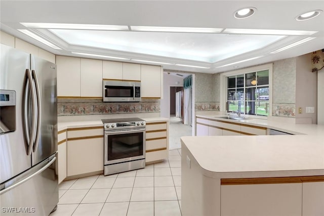 kitchen featuring a raised ceiling, appliances with stainless steel finishes, sink, and kitchen peninsula