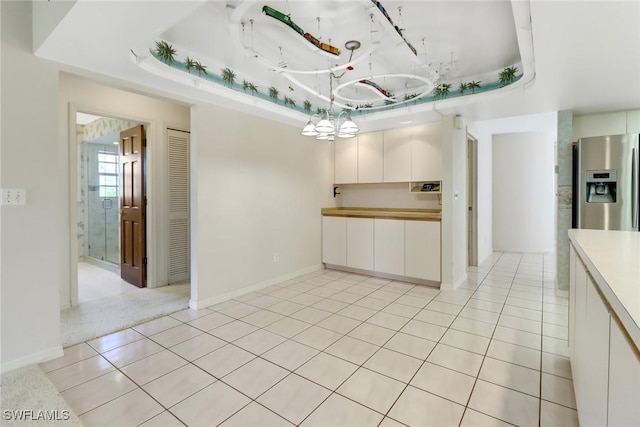 kitchen with light tile patterned floors, a raised ceiling, white cabinets, and stainless steel refrigerator with ice dispenser