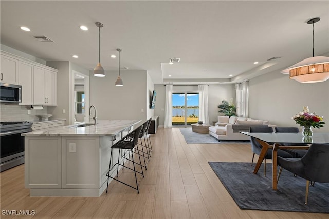 kitchen featuring sink, hanging light fixtures, appliances with stainless steel finishes, light hardwood / wood-style floors, and white cabinets