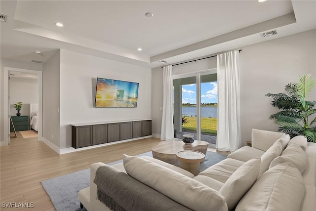 living room with a raised ceiling and light wood-type flooring