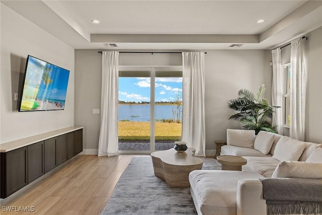 living room with a raised ceiling and light hardwood / wood-style flooring