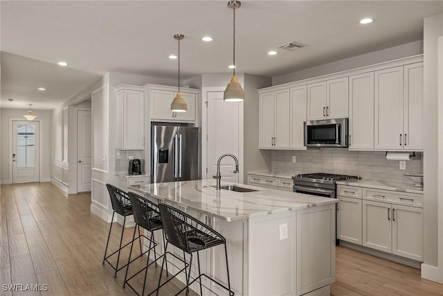 kitchen with sink, a center island with sink, stainless steel appliances, light stone countertops, and white cabinets