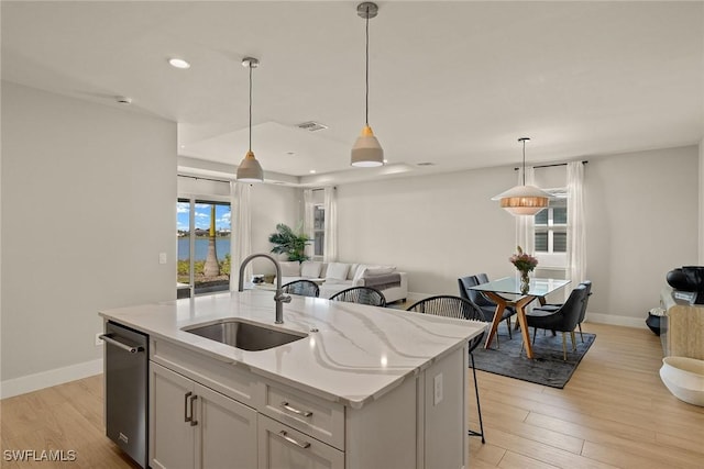 kitchen featuring decorative light fixtures, sink, a kitchen bar, a kitchen island with sink, and light stone countertops